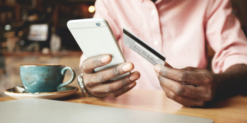 African American man in casual shirt paying with credit card online while making orders via the Internet. Successful black businessman making transaction using mobile bank application.