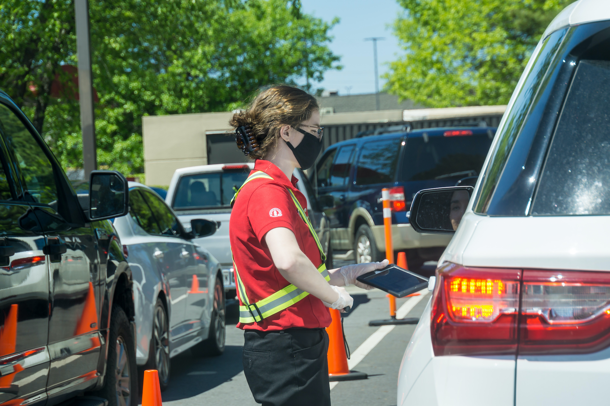 Young youthful fast food worker working at Chick-fil-a drive through amidst cars take orders with tablet.