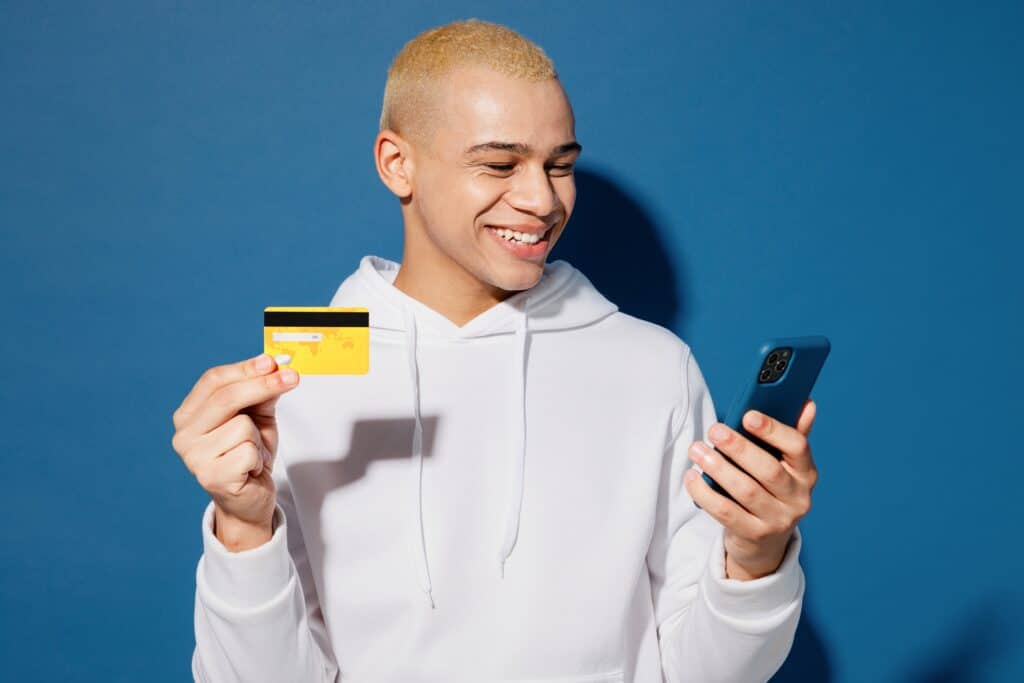 Young man holding debit card using cell phone