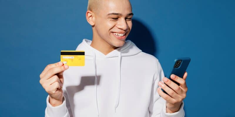 Young man holding debit card using cell phone for digital banking